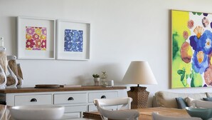 Een eetruimte met een houten tafel, witte stoelen, een witte kast met lades, en een lamp.