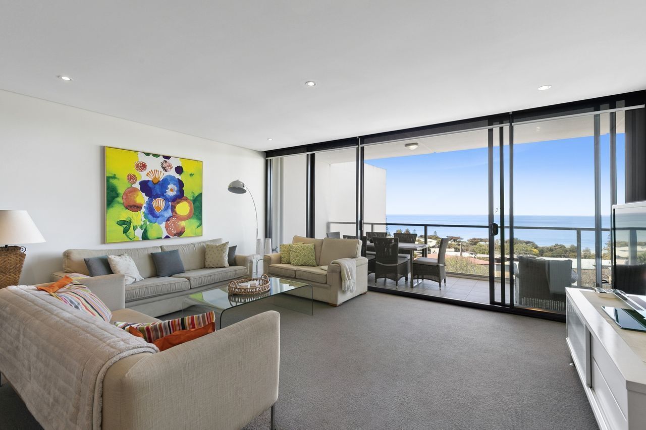 A modern living room with a sofa, armchairs, a coffee table, and a painting on the wall.