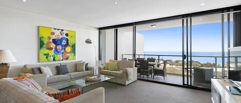 A modern living room with a sofa, armchairs, a coffee table, and a painting on the wall.