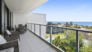 Een balkon met rieten meubilair, een zwembad en uitzicht op zee en woongebied.