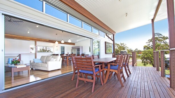 Ein modernes Haus mit einer großen Terrasse, einem Essbereich und einer durch Glastüren einsehbaren Küche.