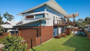 Ein modernes, zweistöckiges Haus mit flachem Dach, großen Fenstern und einer überdachten Terrasse.