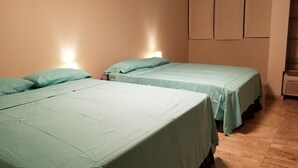 Ein Zimmer mit zwei Betten, jeweils mit hellgrüner Bettdecke und passenden Kissen. Rechts ist eine Wandheizung angebracht und links steht ein kleiner Tisch mit einer Lampe.