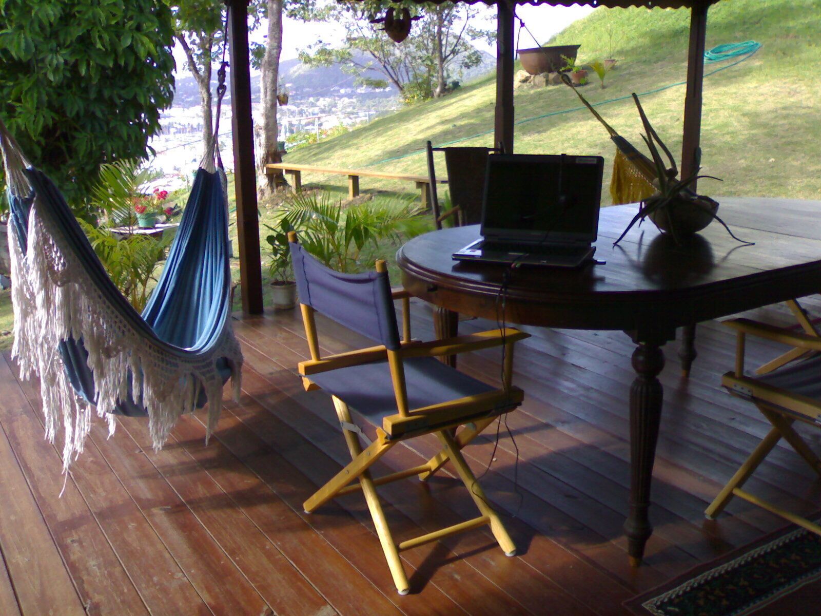 Une terrasse en bois avec un hamac, une table avec un ordinateur portable et des chaises.
