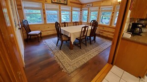 En matplats med ett träbord och stolar, stora fönster och en takfläkt.