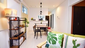 A modern living room with a dining area, a sofa with a cactus pillow, and a kitchen in the background. - Sun Flower (Onna)