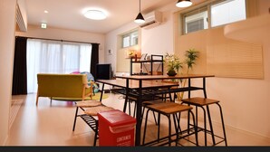 A modern living room with a sofa, a dining table with chairs, a TV, and a red container on the floor. - Sun Flower (Onna)