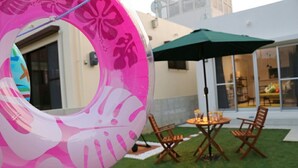 A pink inflatable ring, a green umbrella, and a table with chairs in a grassy outdoor area. - Sun Flower (Onna)