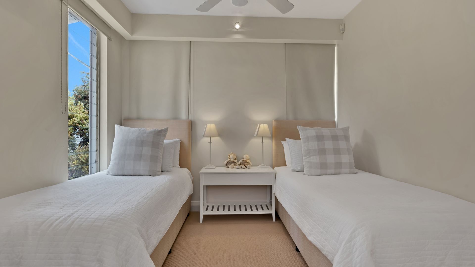 Una habitación de hotel con dos camas, una mesita de noche con lámparas y una ventana que da a las árboles.