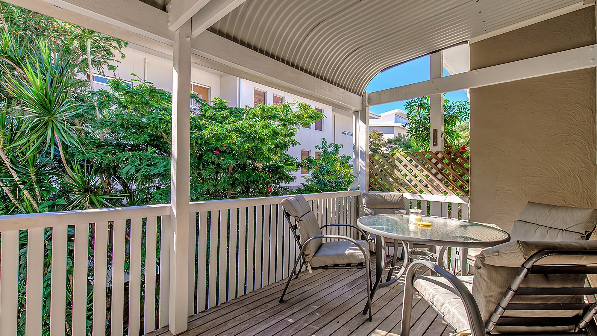 A covered outdoor area with a wooden deck, a glass table, and two chairs.