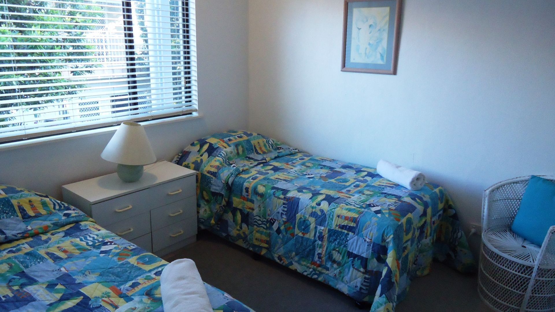 A bedroom with two beds, a nightstand, a lamp, a chair, and a window with blinds.
