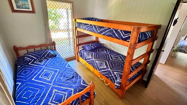 Una cama litera con una colcha de estampado geométrico, un cabecero de madera y una ventana con vistas a zonas verdes.