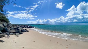 Una playa con costa rocosa, agua azul cristalina y una masa de tierra en la distancia.