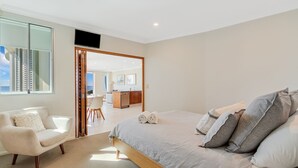 Une chambre moderne avec un grand lit, un coin salon avec un fauteuil et une vue sur la mer, visible à travers une porte vitrée.