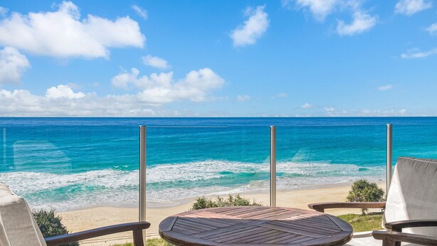 Une vue sur la plage avec une terrasse en bois et deux chaises, donnant sur l’océan.