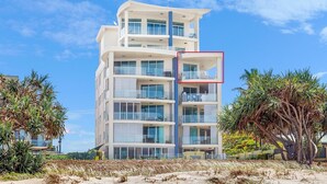 Un hôtel à plusieurs étages, doté de balcons, situé près d’une plage bordée de palmiers.