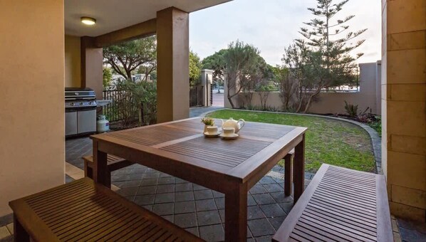 An outdoor patio with a wooden table and benches, a grill, and a small garden area.