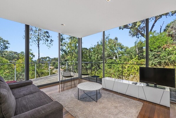 A modern living room with a large window, a flat-screen TV, and a sofa.
