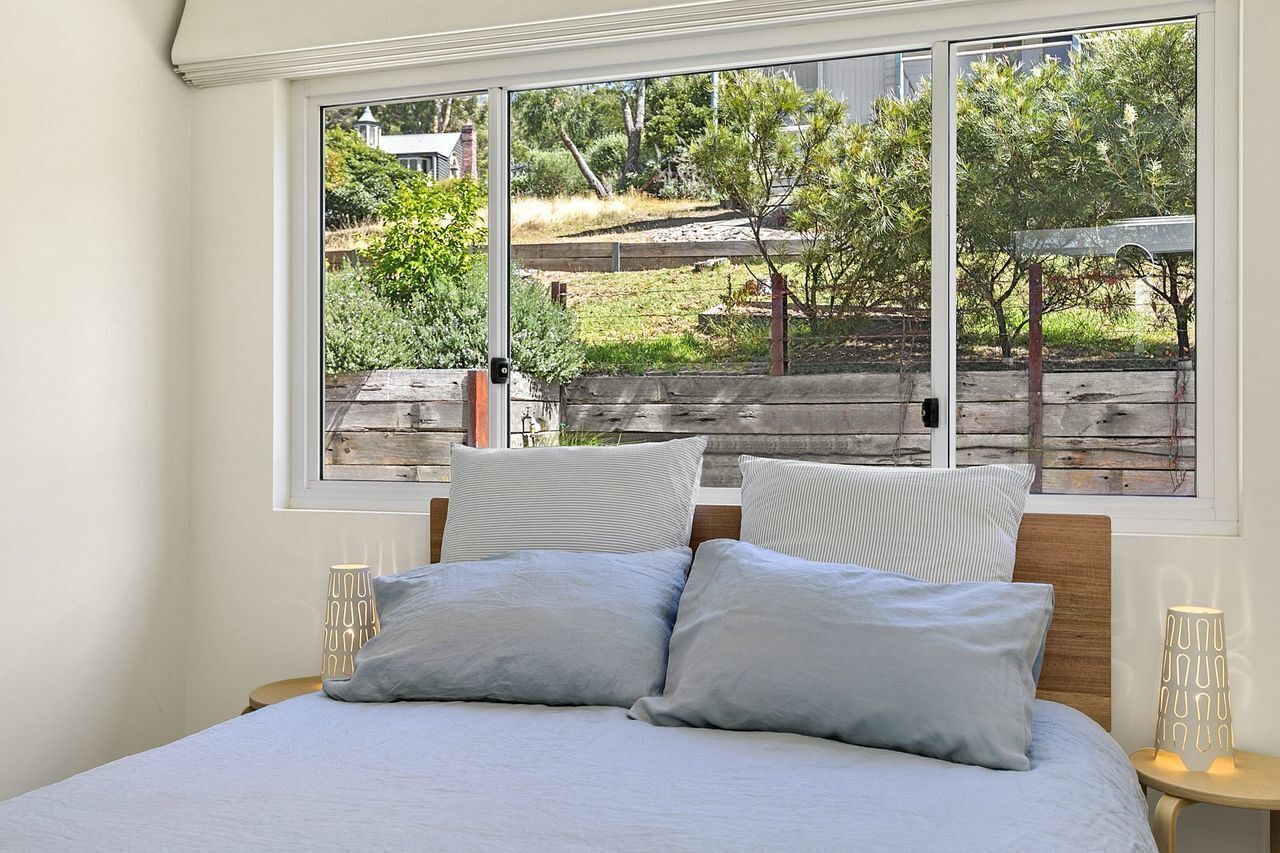 A bedroom with a large window, a bed with two pillows, and a bedside table with a lamp.