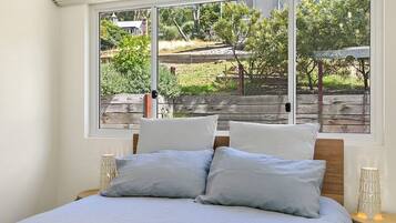 A bedroom with a large window, a bed with two pillows, and a bedside table with a lamp.