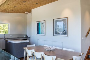 A modern kitchen with a marble countertop, white cabinets, and a wooden ceiling. There is a dining area with a wooden table and white chairs. - Kiara (Lorne)