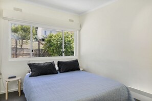 A bedroom with a bed, a window, a radiator, and a small table. - Kiara (Lorne)