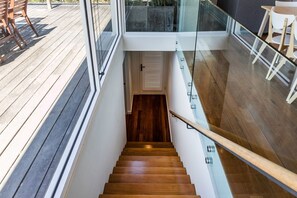 A wooden staircase leading to a lower level with a glass railing, a wooden deck, and outdoor furniture.