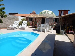 Una piscina con lettini bianchi, un portico coperto e una casa con tetto in tegole.