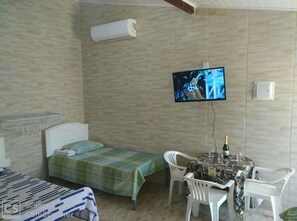 Quarto com cama, mesa e cadeiras, televisão na parede e ar condicionado.