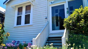 A two-story house with a front porch, a visible number '15' on the door, and a small garden with various flowers. - Luxury Heritage Cottage with Harbour Views in Albany (Albany)