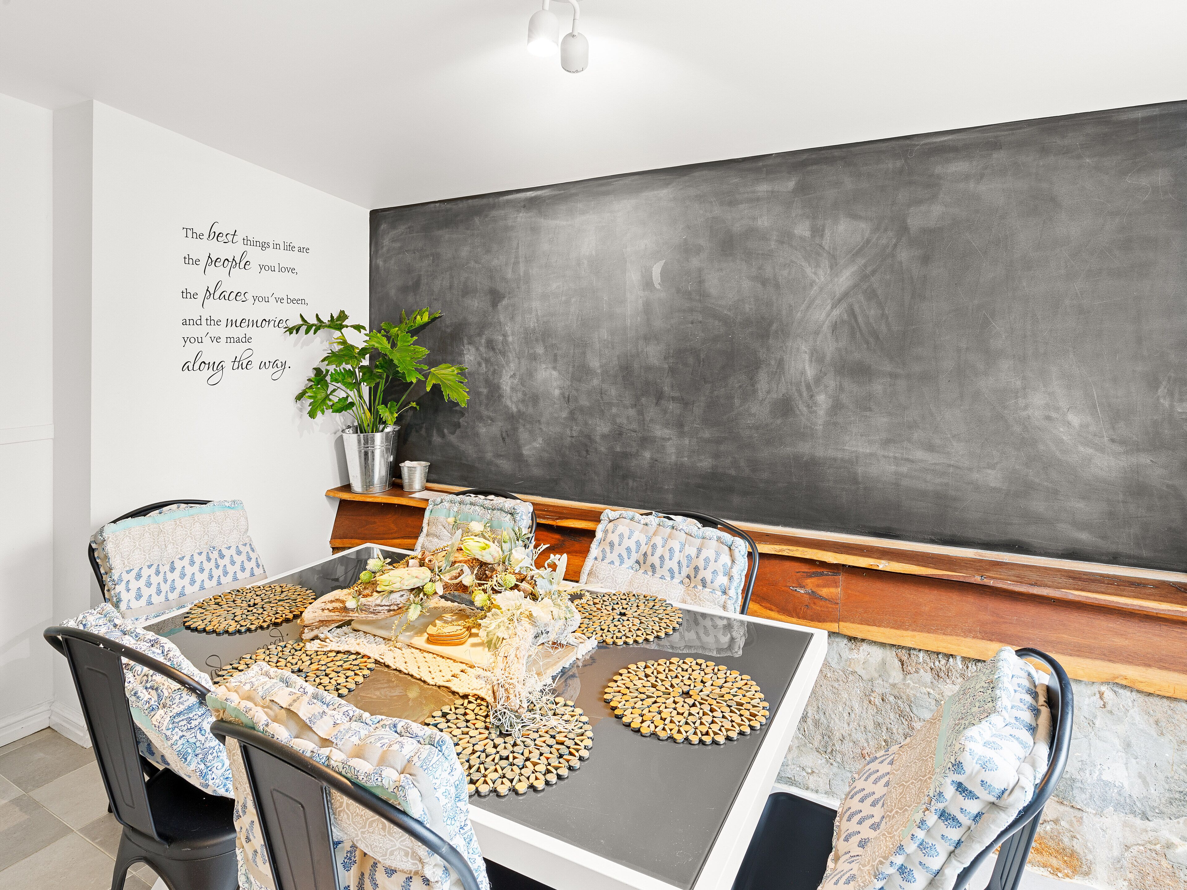 A dining area with a blackboard, a potted plant, and a table set with a placemat and plates.
