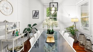 A modern meeting room with a glass table, white chairs, a clock, framed artwork, and potted plants. - Luxury Heritage Cottage with Harbour Views in Albany (Albany)