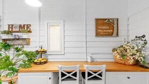 A kitchen with white cabinets, a wooden countertop, two white chairs, a fruit bowl, and a decorative basket with flowers. - Luxury Heritage Cottage with Harbour Views in Albany (Albany)
