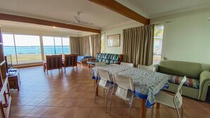 A spacious room with a large dining table, chairs, a sofa, and a view of the sea. - Rio Vista - Burrum Heads - Riverfront - 2BR - Large Yard (BURRUM HEADS)