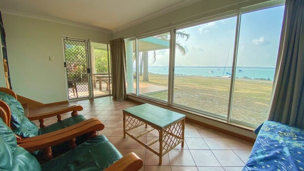 A room with a view of the beach, a wooden bench, a small table, and a bed. - Rio Vista - Burrum Heads - Riverfront - 2BR - Large Yard (BURRUM HEADS)