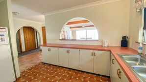 A kitchen with a tiled floor, wooden cabinets, a countertop, and a window with a view. - Rio Vista - Burrum Heads - Riverfront - 2BR - Large Yard (BURRUM HEADS)