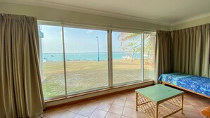 A room with a large window, a bed, a small table, and a view of the beach and sea. - Rio Vista - Burrum Heads - Riverfront - 2BR - Large Yard (BURRUM HEADS)