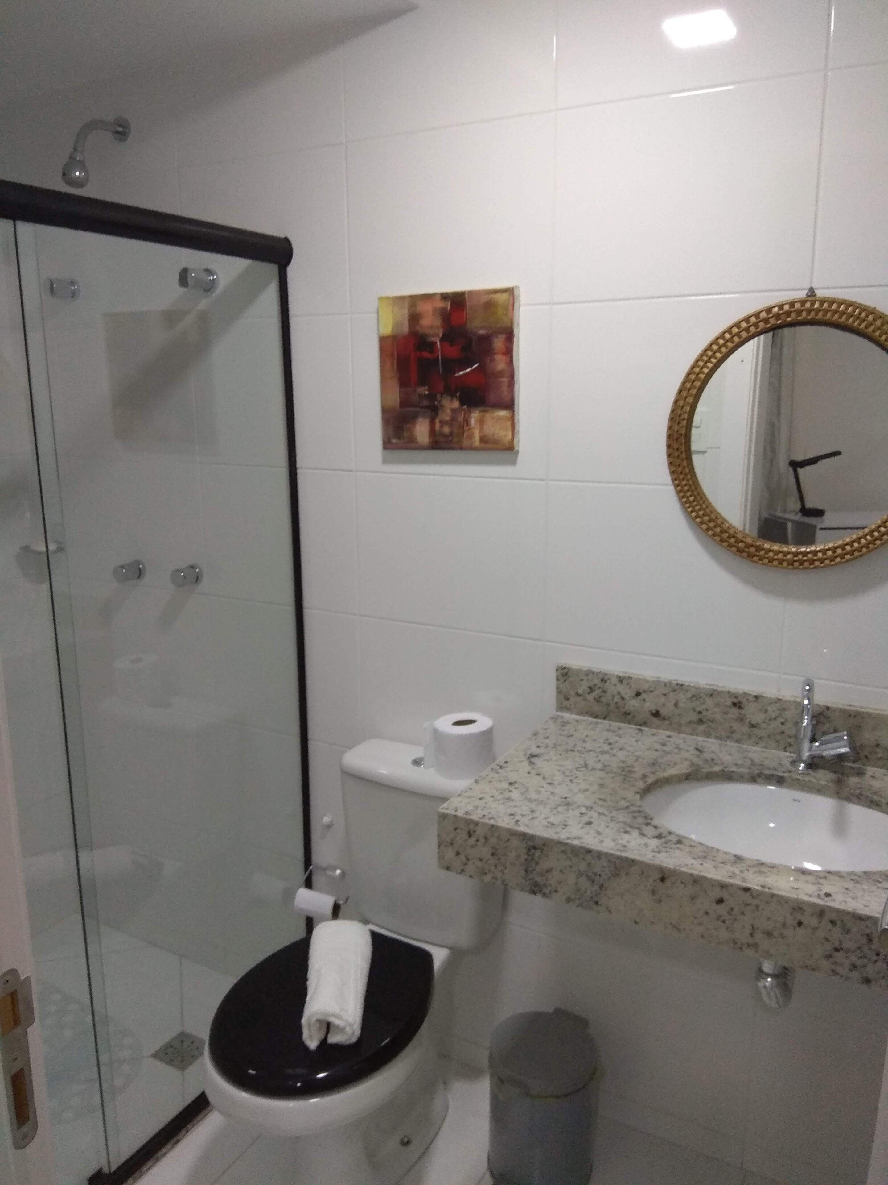 A bathroom with a glass-enclosed shower, a toilet with a black seat, a sink with a granite countertop, and a mirror with a gold frame.
