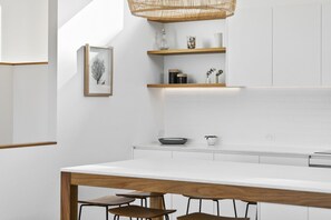 A modern kitchen with white cabinetry, a wooden dining table, and bar stools. - Belvedere Four (Lorne)