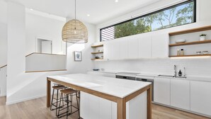 Une cuisine moderne dotée d’un îlot central, de tabourets de bar en bois, de meubles blancs et d’une grande fenêtre au-dessus de l’évier.