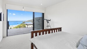 Une chambre à coucher avec un lit, un télescope et une vue sur la mer, visible à travers une porte-fenêtre coulissante.