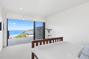 A bedroom with a bed, a telescope, and a view of the sea through a sliding glass door. - Belvedere Four (Lorne)