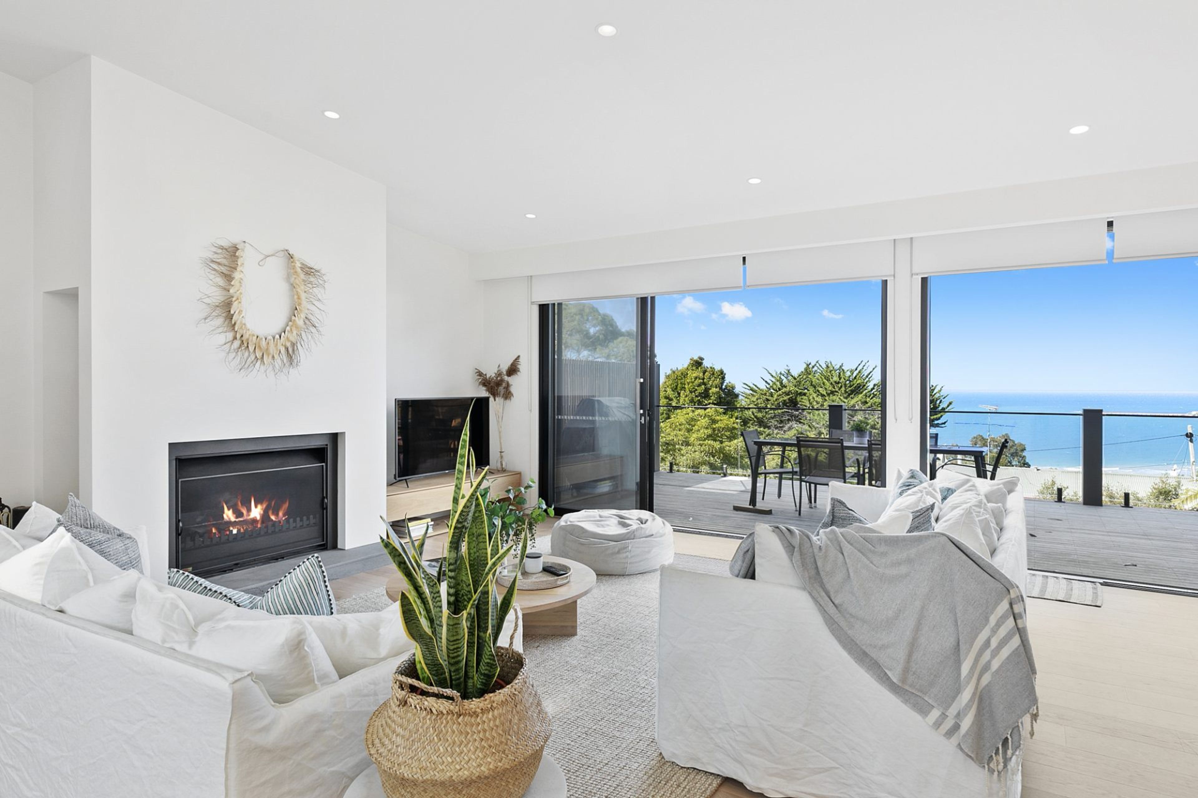 A modern living room with a fireplace, white furniture, and a view of the sea.