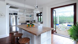 Une cuisine moderne dotée d’un îlot central en bois, d’appareils électroménagers en acier inoxydable et d’une grande fenêtre offrant une vue sur l’extérieur.