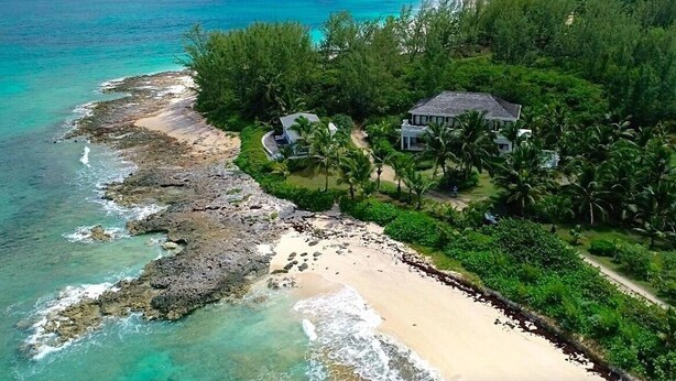 Vue aérienne d’une propriété située sur la côte, avec une plage, un littoral rocheux et une végétation luxuriante.