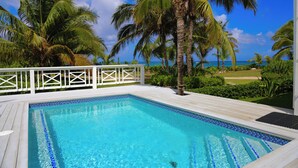 Une piscine rectangulaire aux carreaux bleus, entourée d’une terrasse en bois et de rampes blanches.