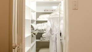 Un petit dressing étroit avec des étagères blanches, une robe suspendue et des serviettes pliées avec soin.