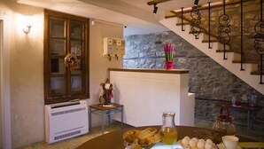 A cozy room with a stone wall, a wooden staircase, a small table with snacks, and a decorative wreath on the door. - Villa 4 Bed & Breakfast (Berat)