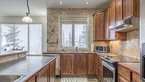 Una cocina moderna con armarios de madera, horno empotrado y un ventanal con vistas a árboles nevados.