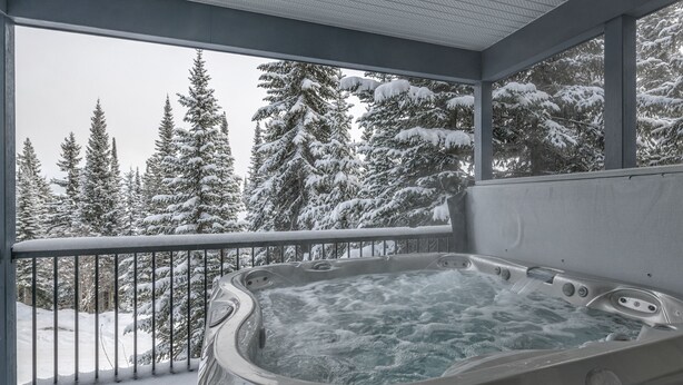 Un jacuzzi en un balcón con vista a un bosque nevado.